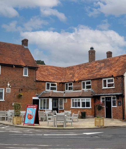 The exterior facade, signage, and seating area at The Vine Inn in Ower, with small trees in wooden planter boxes.