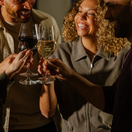 An image of 4 customers enjoying glasses wine and celebrating with a cheers stood within the interior of The Crown.