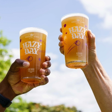 Two hands, each holding a pint of Hazy Day in the air,  with the sky as a backdrop.