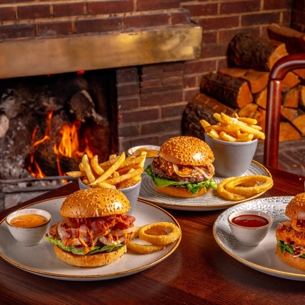 An advertising image of a 3 plated burgers with onion rings, fries and sauce available at Urban Core venues.