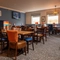 The interior restaurant seating area at The Heron in Havant; with wooden tables and chairs, a blue velvet booth seat against one wall, two windows at the far end of the room, and a TV on the wall.