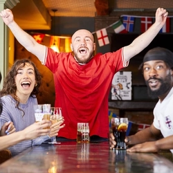 A mixed group of people sitting at an indoor table, enjoying watching sport and drinks.