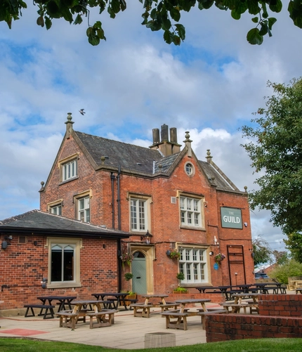 An image of the exterior facade and beer garden seating area at The Guild.