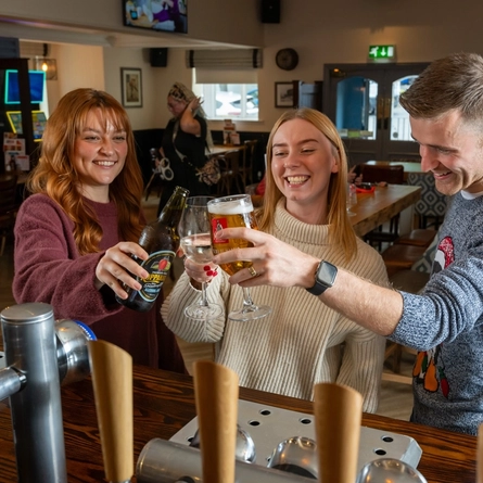 A group of people stood at a bar raising their drinks in a toast.