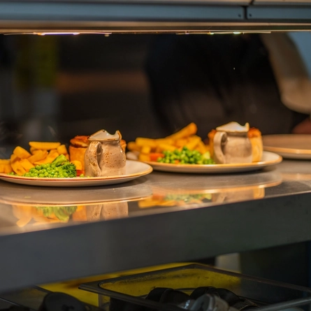 An image showing various plated dishes sat on an interior  food pass-through counter cabinet at a Chef & Brewer venue.