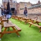 The exterior beer garden seating area of The Merlin in Edinburgh, with wooden picnic benches and shade umbrellas.