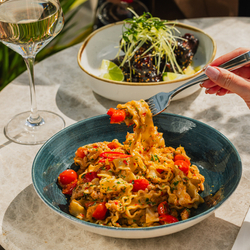 A lifestyle image showing a person enjoying a bowled pasta dish and glass of white wine at a Crafted venue.