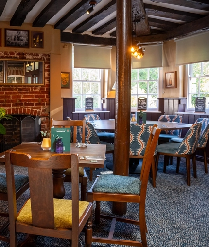 The interior restaurant seating area of The Fox, with a brick fireplace, and wooden beams on the ceiling.