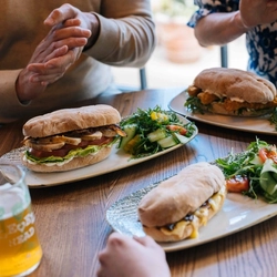 A close up image showing 3 sandwich dishes being enjoyed by people sat at a table within the interior restaurant seating area at a Heritage venue.