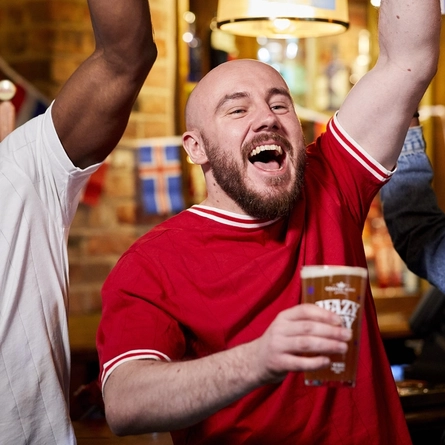 A mixed group of people holding a drink and cheering.