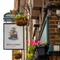 A close up view of the pub sign hanging in between two flower baskets on the exterior wall of the Royal George. The sign features an illustration of a large ship sailing on the sea above the words "Royal George, Euston", on a white background.