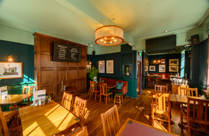 The upstairs interior restaurant seating area at the Coach & Horses in Soho; with wood panelled walls, upholstered booth seats, and a TV on the wall.
