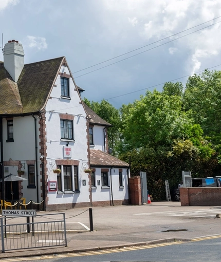 A view from across the road of the exterior facade, signage, seating area, and car park of The Amington in Tamworth.