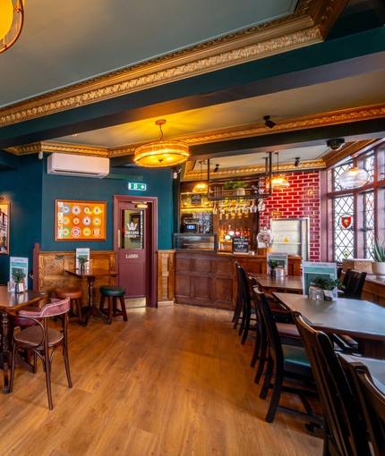 An interior restaurant seating area at The Golden Lion, with a TV on the wall, upholstered booth seats, golden cornices, and a small bar.