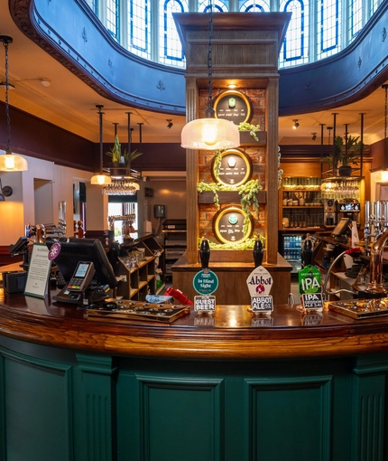 A close up view of the U-shaped bar at the Golden Hind in Cambridge, with leaded windows visible through an oval shaped opening in the ceiling above the bar, mirroring the shape of the counter.