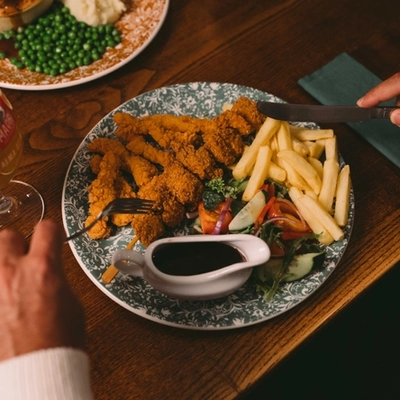The hands of a person holding cutlery above a plated meal on a festive decorated wooden table.