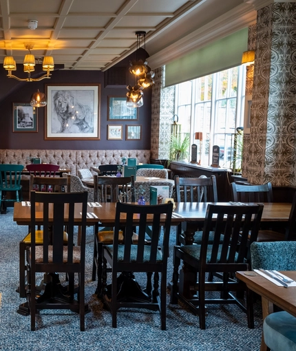 The interior restaurant seating area of The White Lion in Frenchay, with an upholstered booth seating area, a fireplace, and framed artwork on the walls.
