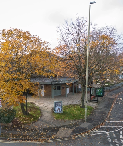 An aerial view of the exterior facade and signage of The Longship, with two large trees in front of the building, and a view of the rest of the street.
