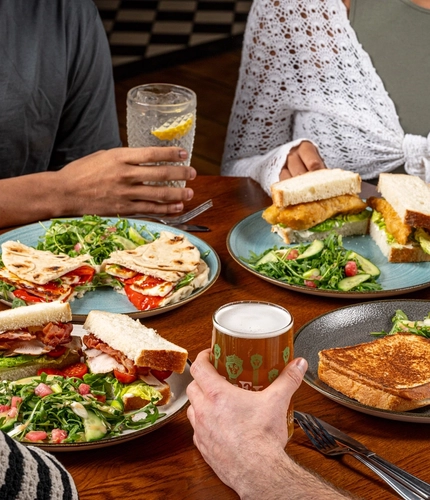 A table of food and drinks with some hands holding the drinks.