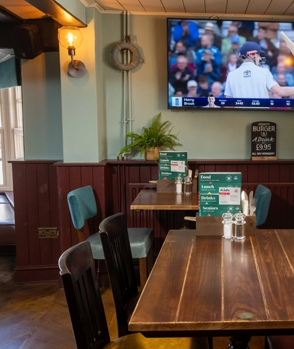 An interior restaurant seating area at The Ship; with plants and a box of board games sitting on the windowsill, and a TV on the wall.
