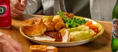 An image of gravy being poured over a Sunday Roast with various drinks within the interior restaurant and seating area at a Hungry Horse venue.
