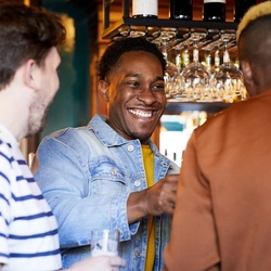 A group of people in a pub bar area, laughing together and holding drinks.