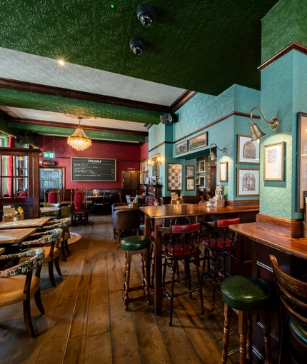 The bar and interior restaurant seating area at the King's Head, with dark wood floors; textured green wallpaper on the ceiling; and upholstered chairs and bar stools.