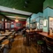The bar and interior restaurant seating area at the King's Head, with dark wood floors; textured green wallpaper on the ceiling; and upholstered chairs and bar stools.