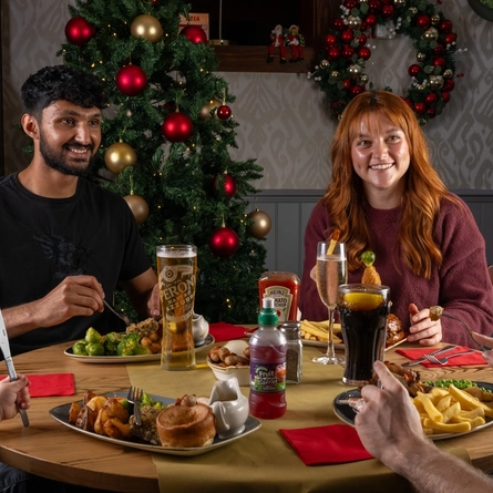A group of people seated around a festive decorated table with plated meals in front of them.