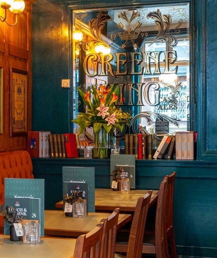 The wood panelled interior restaurant seating area of the Lucas Arms in London, with upholstered booth seating, books on a shelf, and framed artwork on the wall.