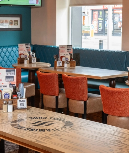 An interior restaurant seating area at The Tamar in Crownhill, with upholstered bench and booth seating, and a TV on the wall.