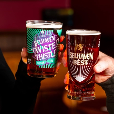 A close up view of two hands, one holding a glass of Belhaven Twisted Thistle, and the other holding a glass of Belhaven Best.