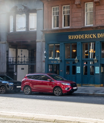 A view from across the road of the exterior facade and signage of the Rhoderick Dhu in Glasgow, with golden lanterns hanging on the walls.