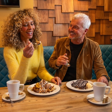 An image showing 2 people sat at a table enjoying dessert dishes and hot drinks at a Flaming Grill venue.