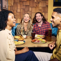 An image showing 4 friends sat at a table enjoying food and drinks within the interior restaurant seating area at a Flaming Grill venue.