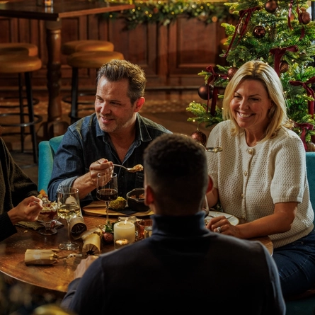 An image of people enjoying festive desserts and drinks within the interior restaurant seating area with fireplace at The Watermill.
