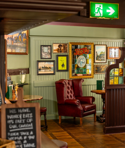 An interior restaurant seating area at The London Apprentice, with upholstered chairs and barstool seats, wooden flooring, and framed artwork on the wall.