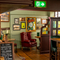 An interior restaurant seating area at The London Apprentice, with upholstered chairs and barstool seats, wooden flooring, and framed artwork on the wall.