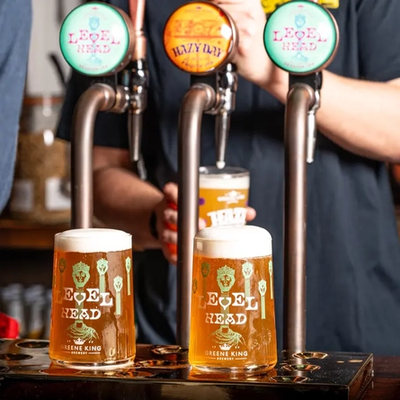 A barman pouring pints of Greene King beers