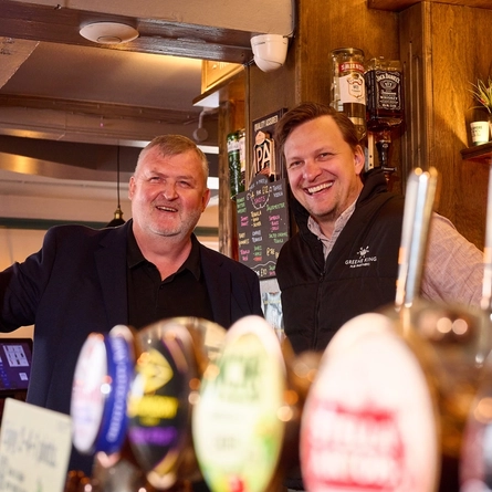 A Pub Partners image showing 2 people stood behind the bar at the Hertford Bell.