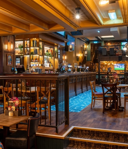The bar and interior restaurant seating area of the Old School House, with wood panelling on the walls, and TVs above the bar.