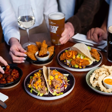 A close up image of people at a table within the restaurant area enjoying small plates dishes and drinks available at Urban Social venues.