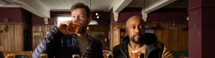 Two men drinking at the bar with pint glasses in hand.