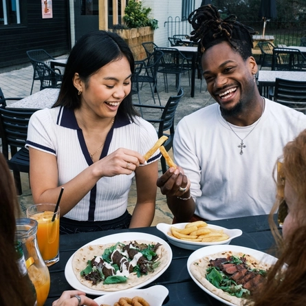 Friends enjoying a meal and drinks in the exterior seating area and beer garden from the new Spring/Summer menu at Flaming Grill.