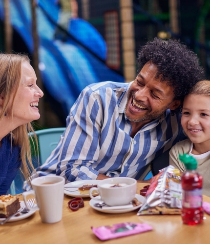A family enjoying cake and hot drinks at a table in a Wacky Warehouse.