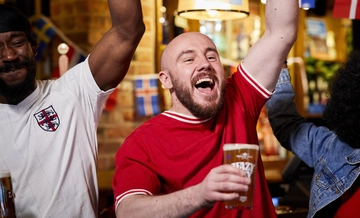 A mixed group of people holding a drink and cheering.