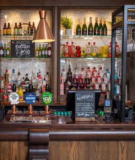 A close up view of the bar inside The Man On The Moon, showing the beer taps, bottles of various wines and spirits on shelves, and glasses hanging in racks above the bar.