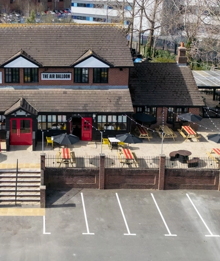 An aerial view of the exterior facade, signage, beer garden seating area, and car park of The Air Balloon, with steps leading up to the entrance.