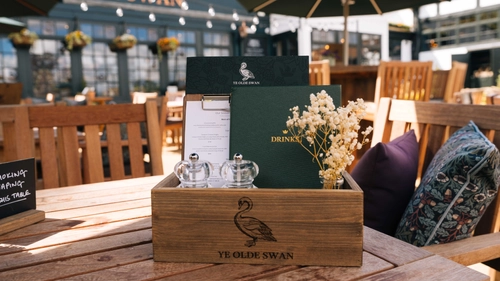 A close up view of a wooden table in the exterior beer garden seating area of Ye Olde Swan. A wooden box sits on the table and contains menus, salt and pepper mills, and a table ornament.