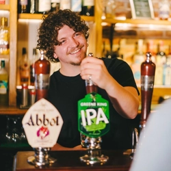 A man behind a bar is pouring a pint of Greene King IPA.